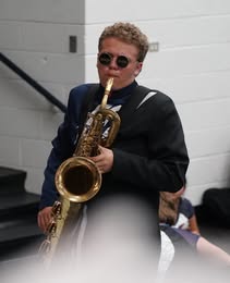 Caden wearing sunglasses and a blazer while playing saxophone